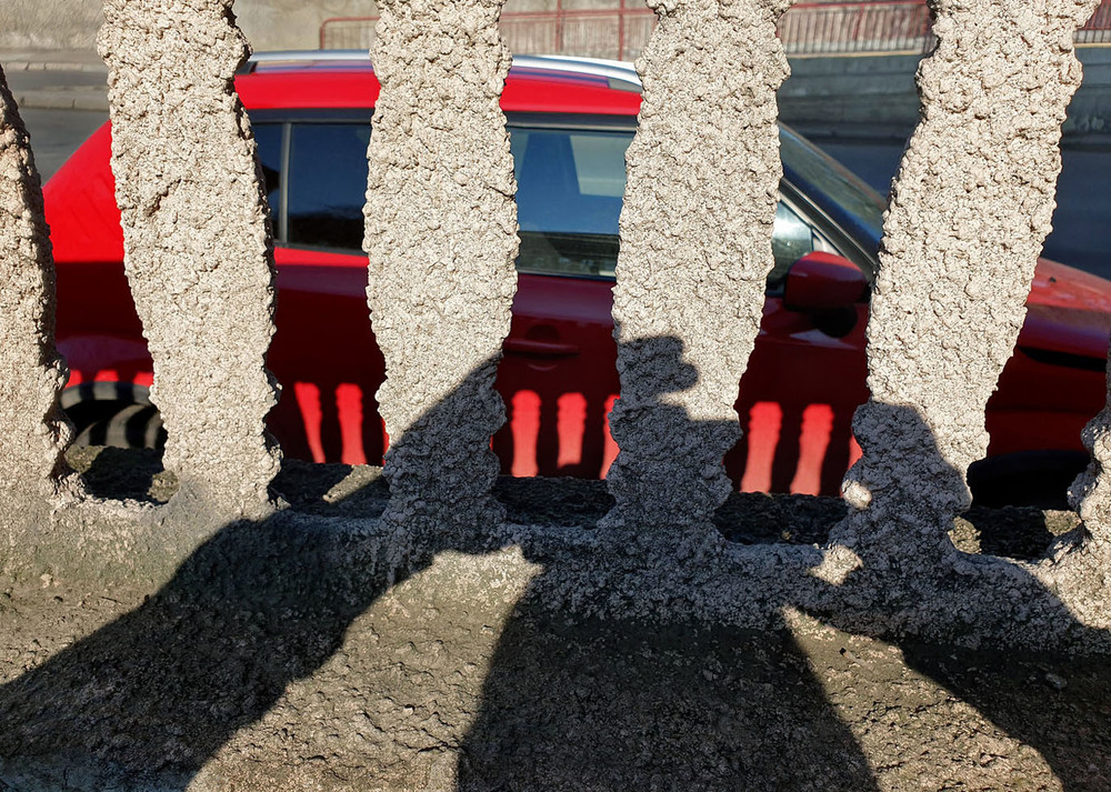 Фотографія Тень фотографа на заборчике через который падает свет на красное авто. / Синельников Александр / photographers.ua