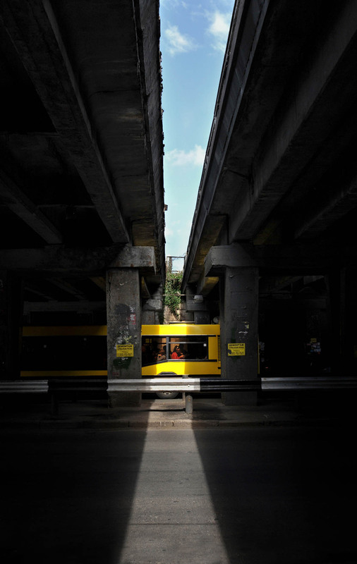 Фотографія девушка в красной кофте, едущая в желтом автобусе под мостом, в полоске солнечного света / Синельников Александр / photographers.ua